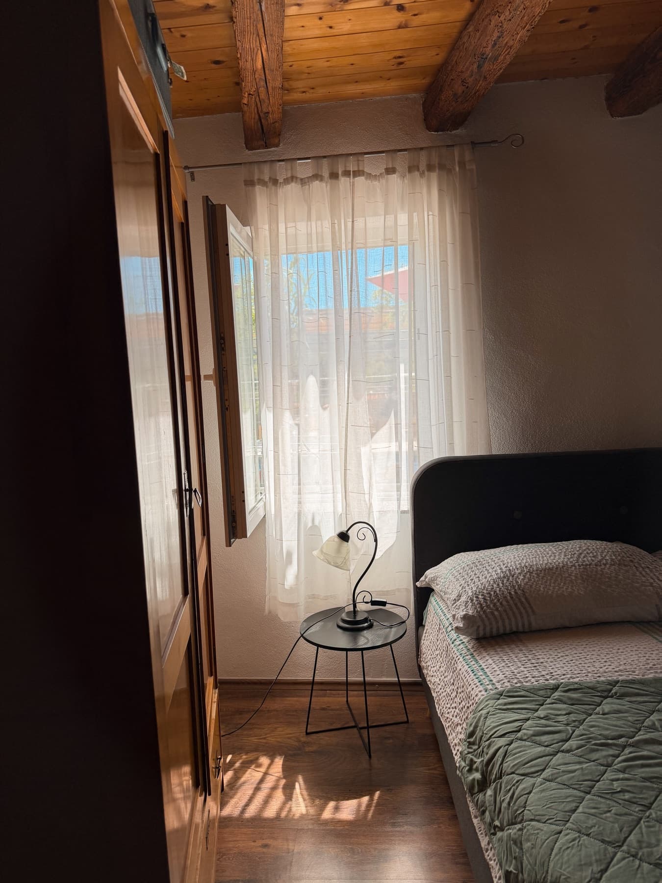 Krevet u apartmanu uz prozor, noćni stolić i lampu pokraj uzglavlja