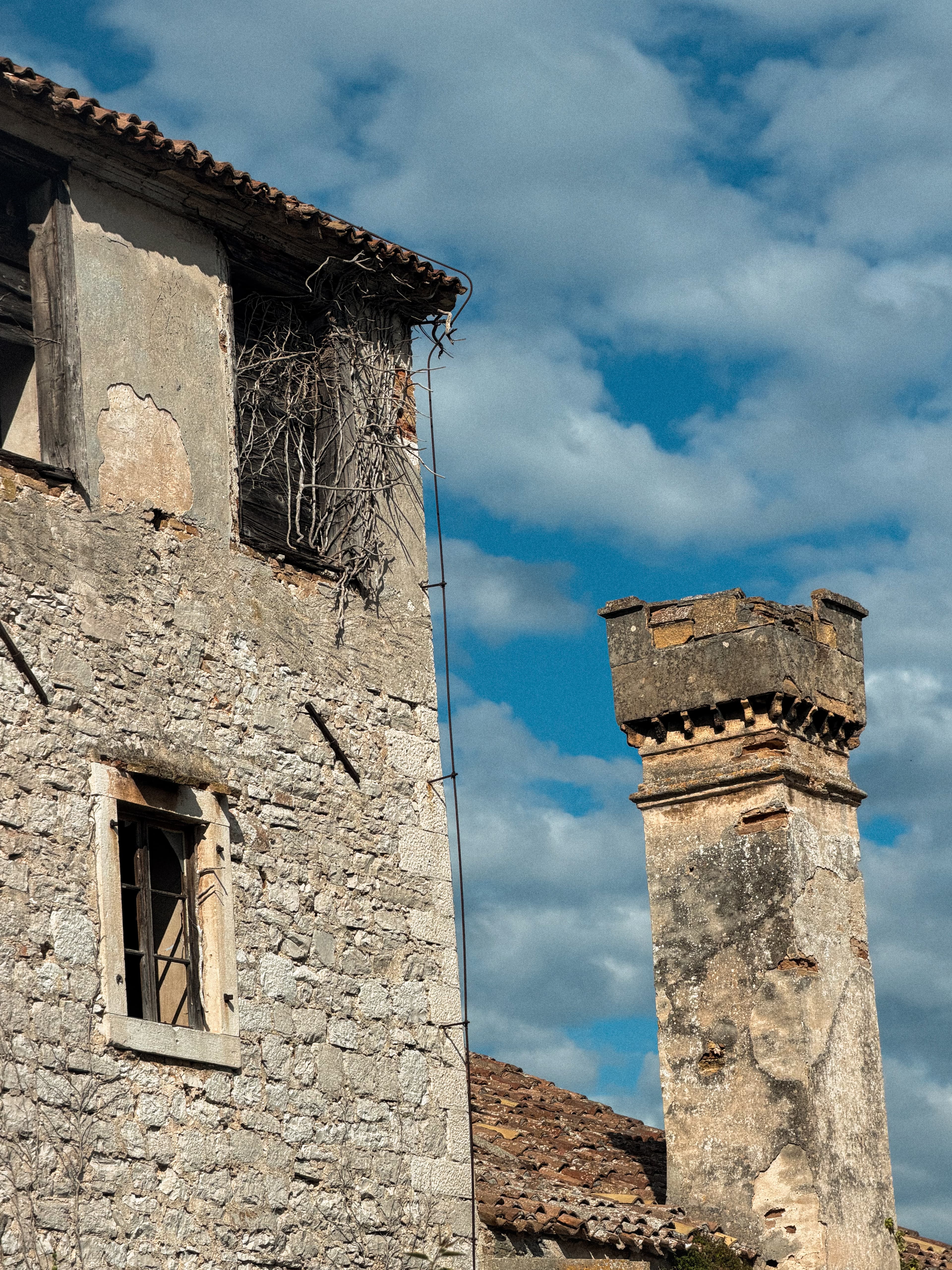 Stara kamena kuća s oštećenim prozorom i dotrajalim dimnjakom, primjer objekta koji čeka odluku o rušenju ili renovaciji
