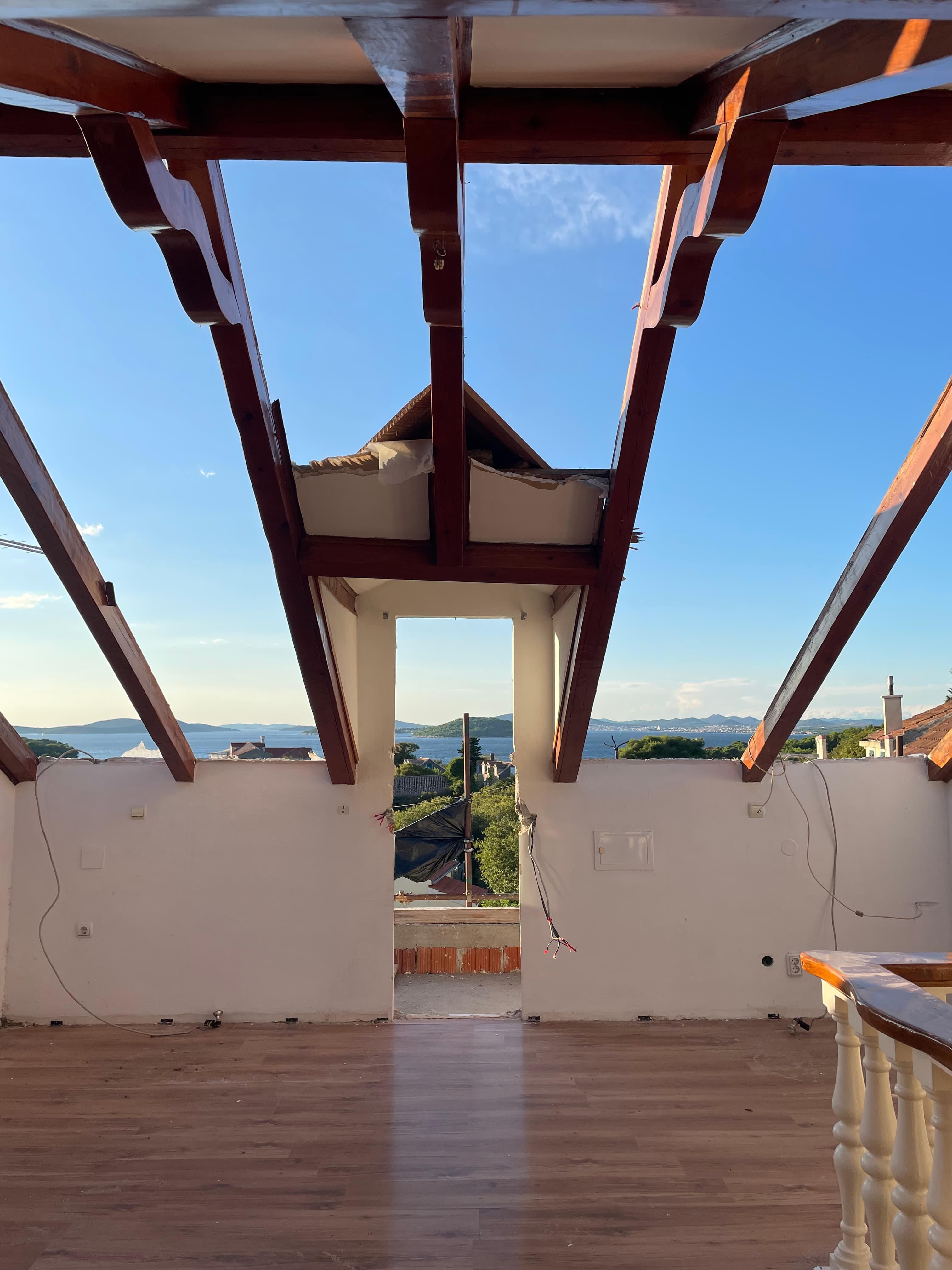 Kamena kuća tijekom renovacije, s novom drvenom krovnom konstrukcijom postavljenom na postojeće kamene zidove i pogledom prema moru