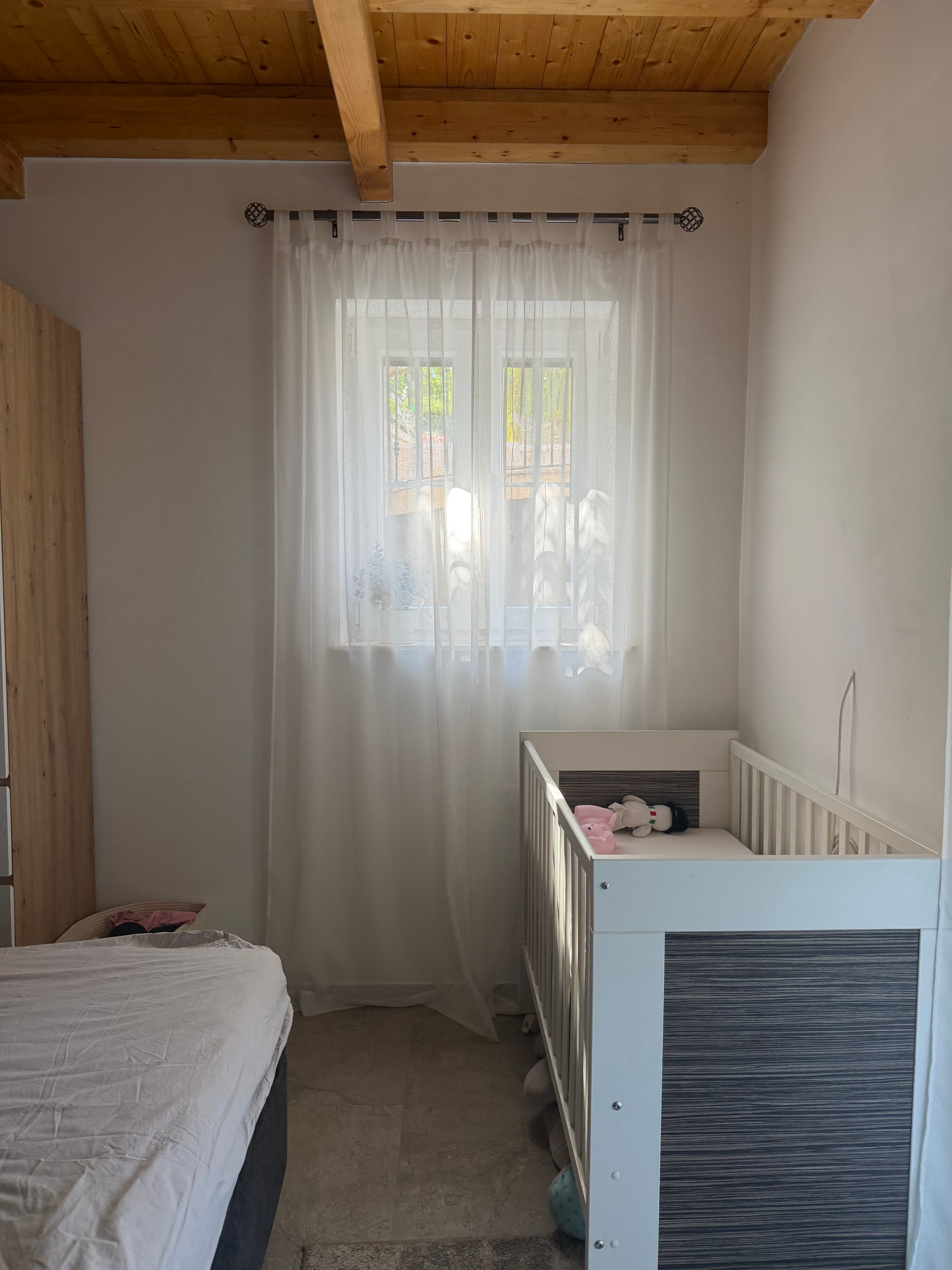 Kinderbet pomaknut ispod prozora sa svjetlom koje prolazi kroz zavjese